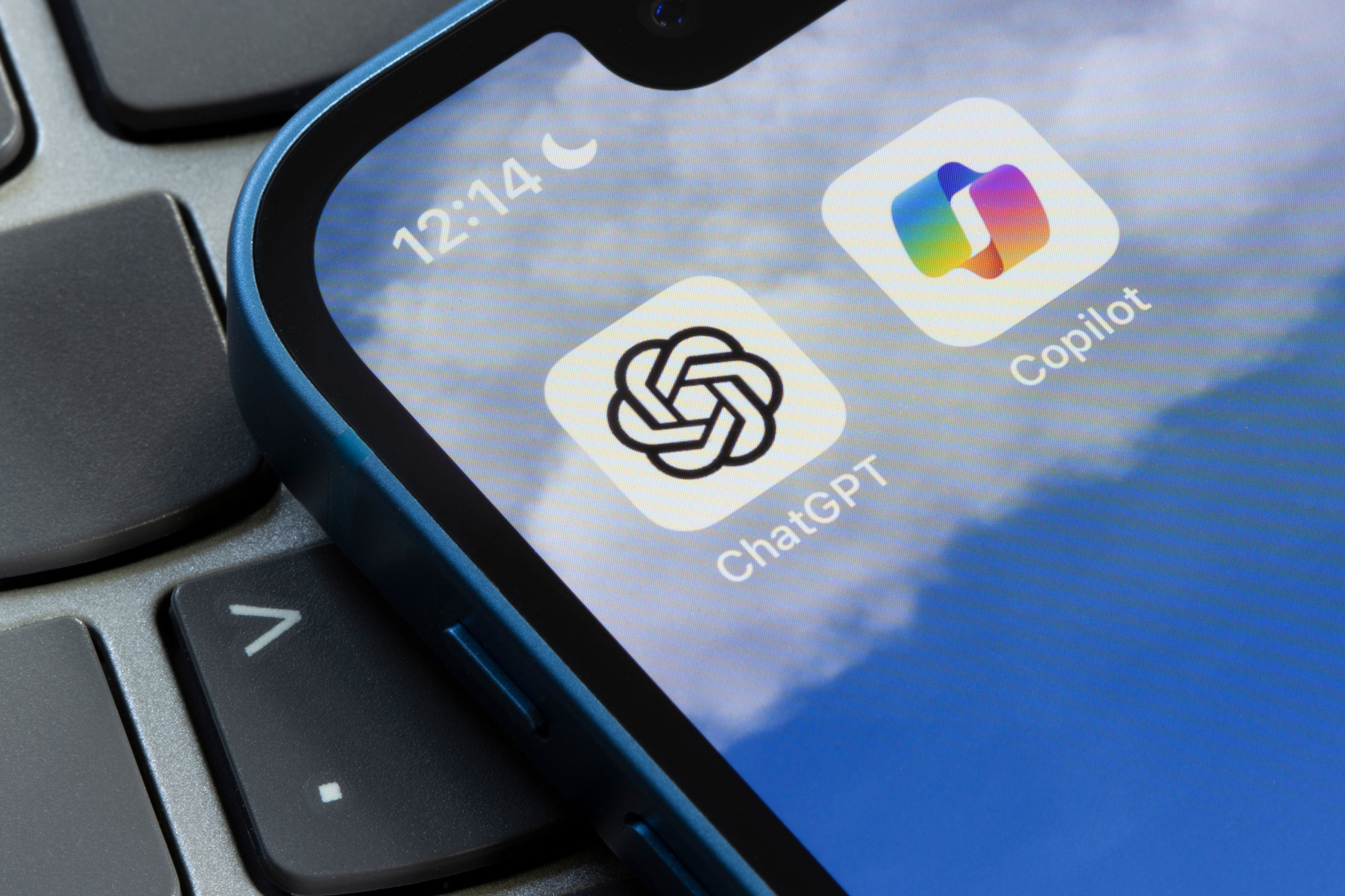 Ein Smartphone, worauf App Symbolen von ChatGPT und MS Copilat zu sehen sind, liegt auf einer Laptoptastatur