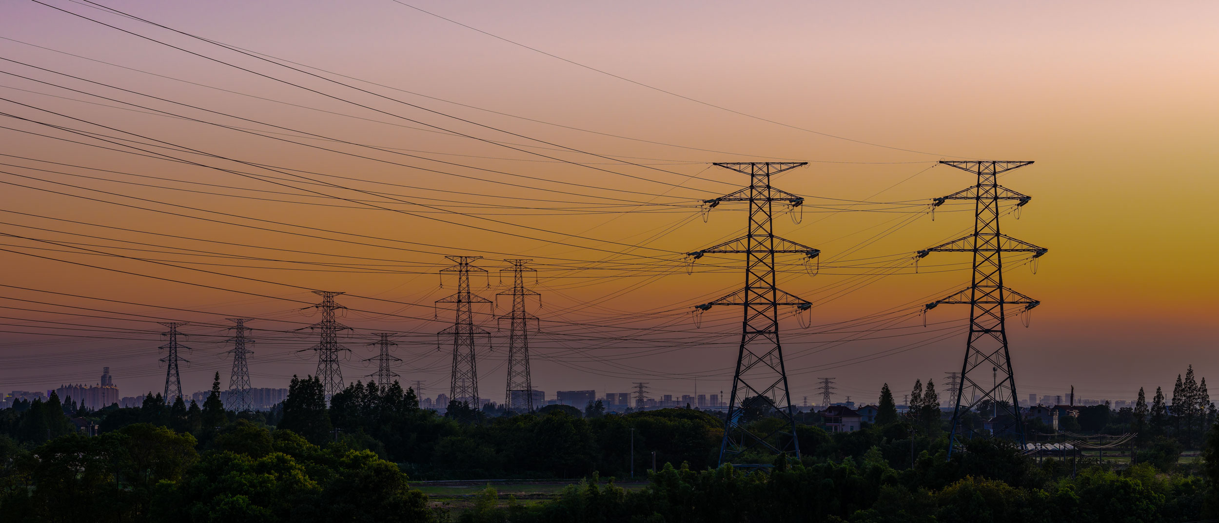 Strommasten bei Sonnenuntergang in einer Landschaft vor einer Stadt
