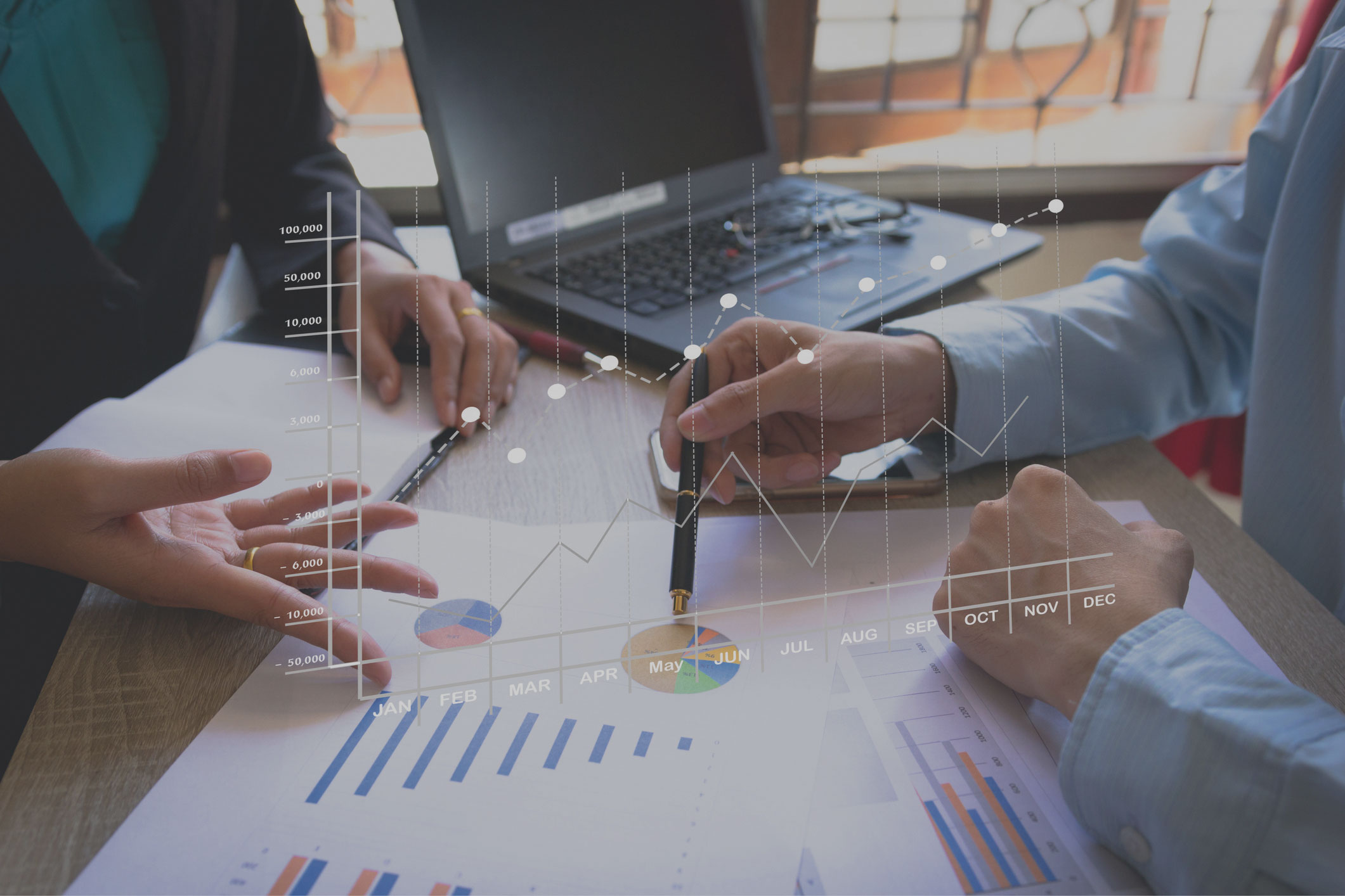 Zwei Menschen sitzen am Tisch und analysieren Tabellenm Im Vordergrund sieht man Finanzcharts.