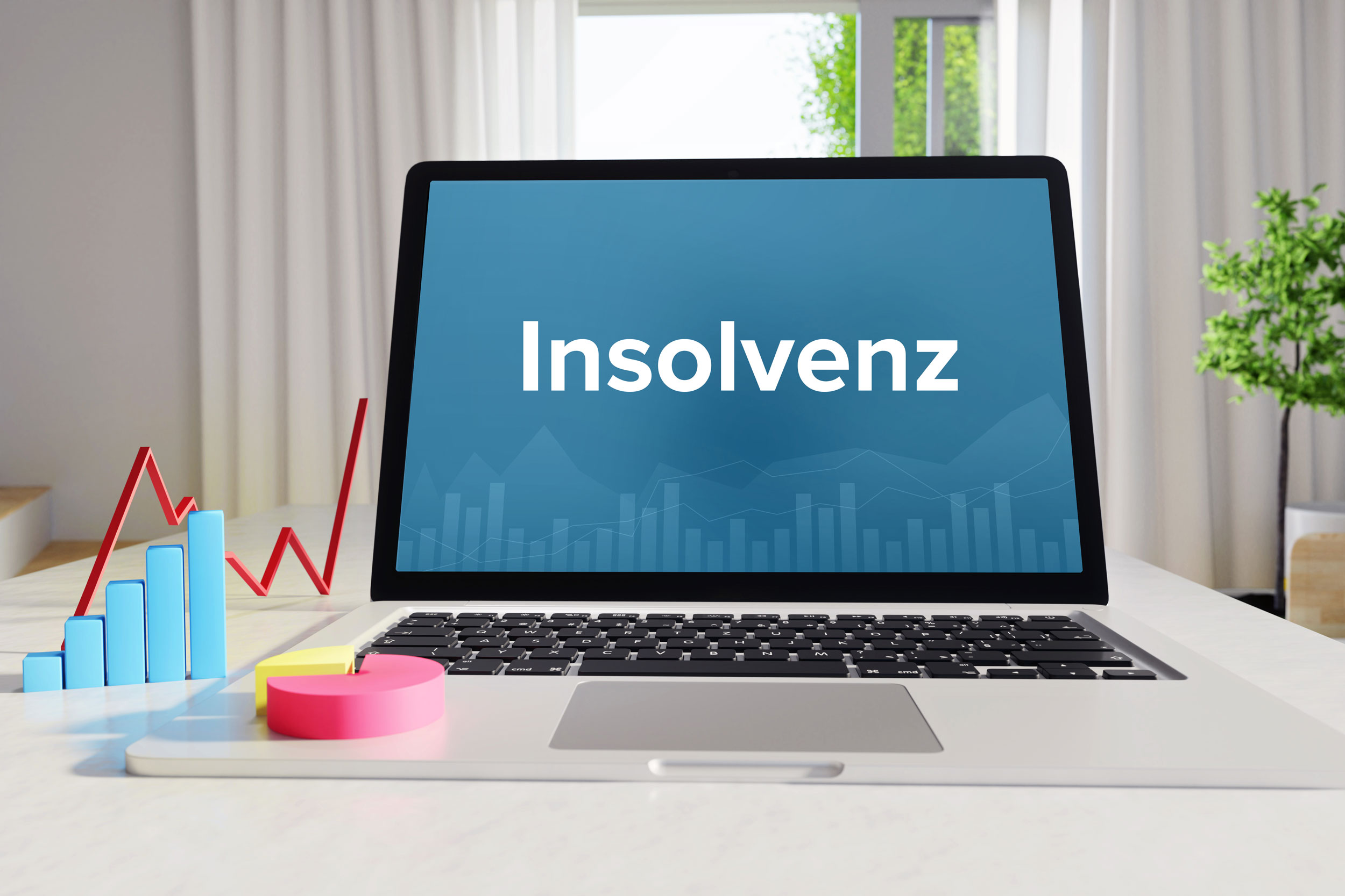 Auf einem Tisch steht gemeinsam mit einigen Grafikelementen ein Laptop, auf dessen Bildschirm Insolvenz geschrieben steht.