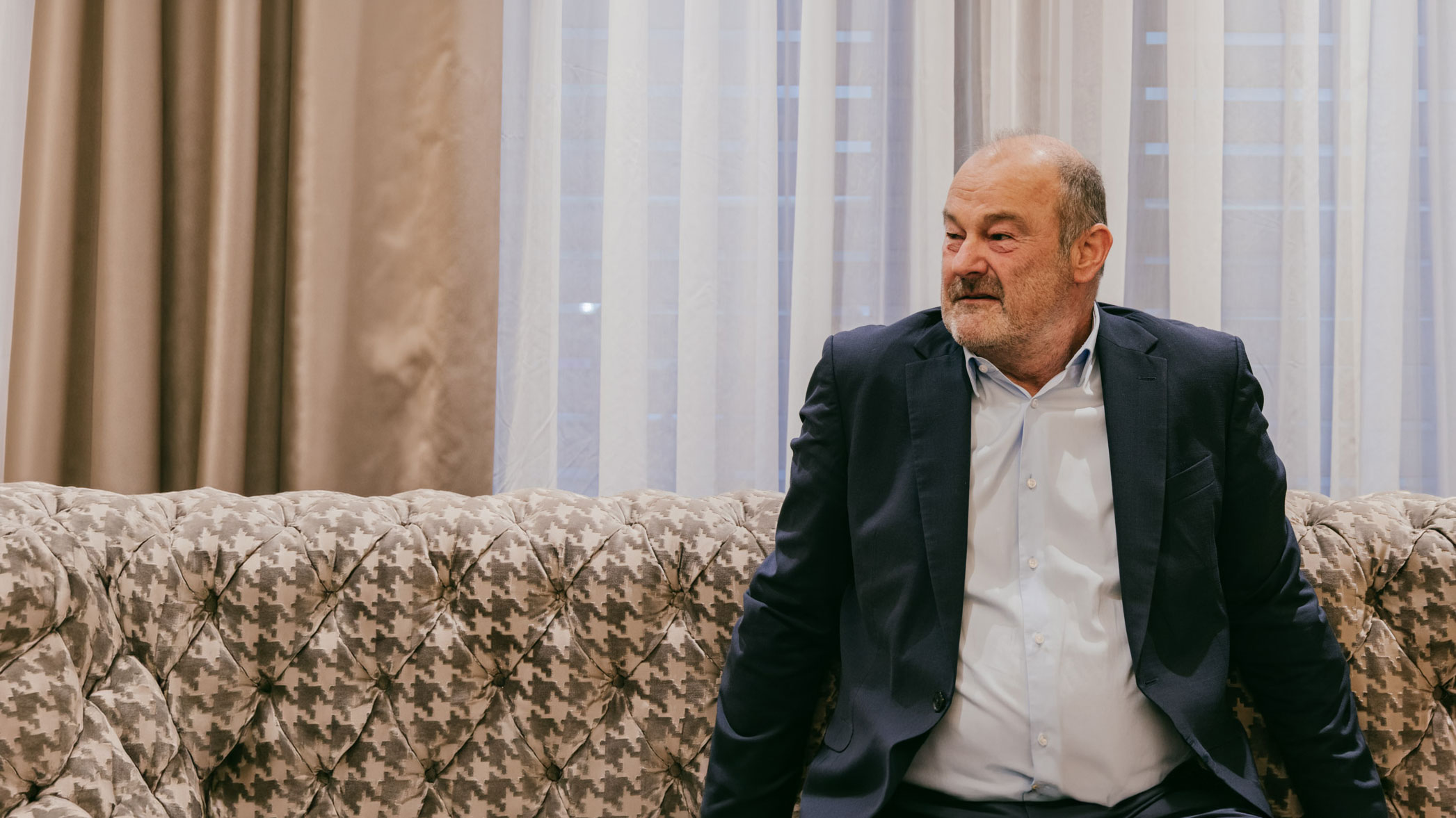 Ein Portrait von Dr. Thomas Müller auf einer karierten Couch von einem weißen Vorhang