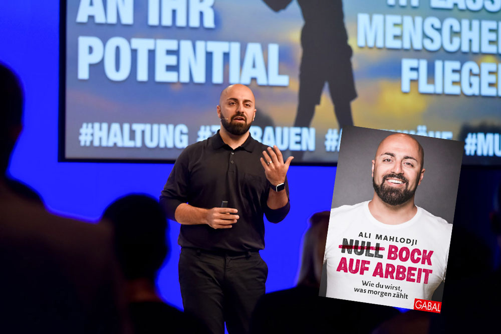 Ali Mahlodji Vor Einem Publikum vor einem großen Bildschirm