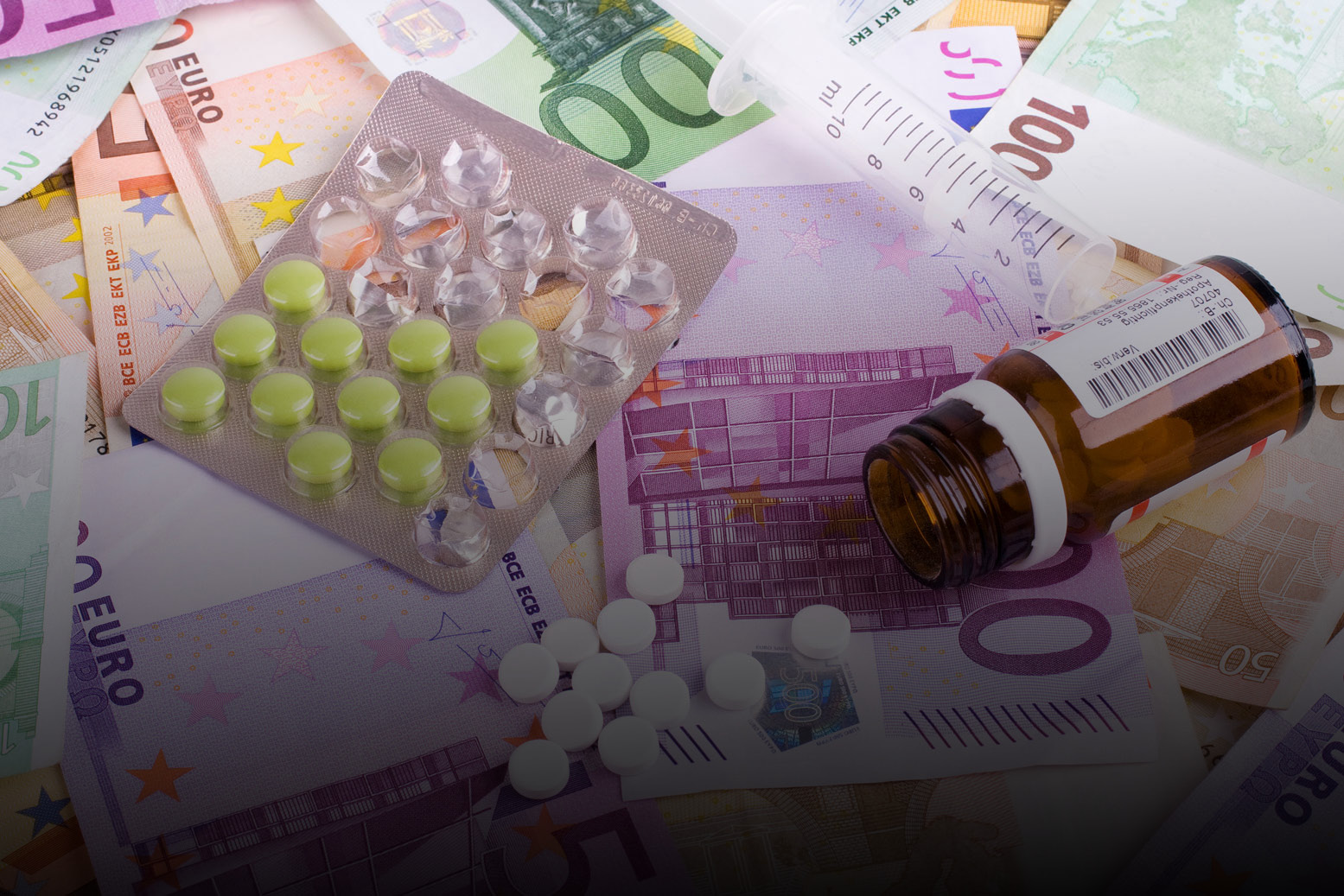 Ein Tablettenbriefchen und eine kleine Tabletten-Flasche liegen auf Euro-Scheinen. 