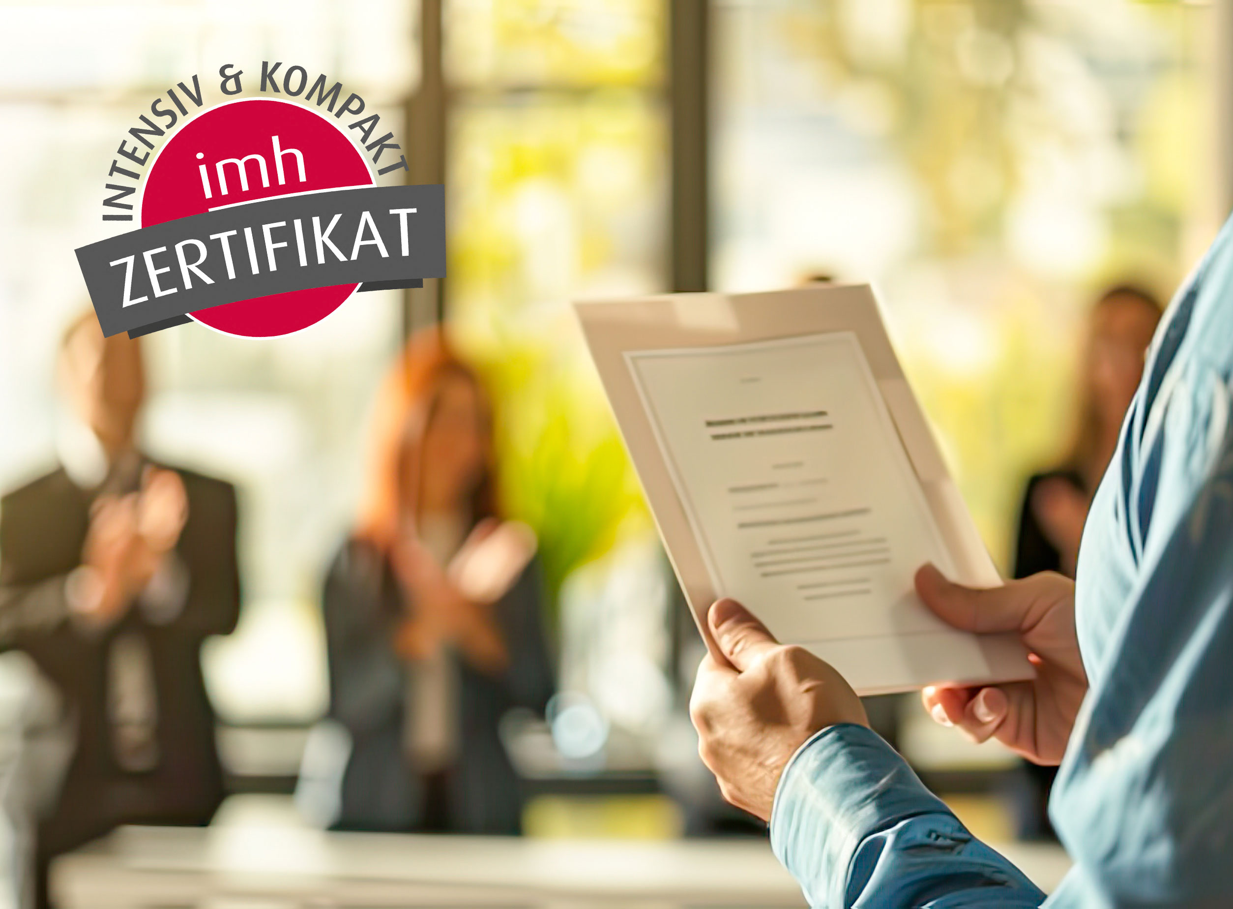 Mann hält Zertifikat, Kolleg:innen applaudieren im Hintergrund, imh Zertifikatslehrgang