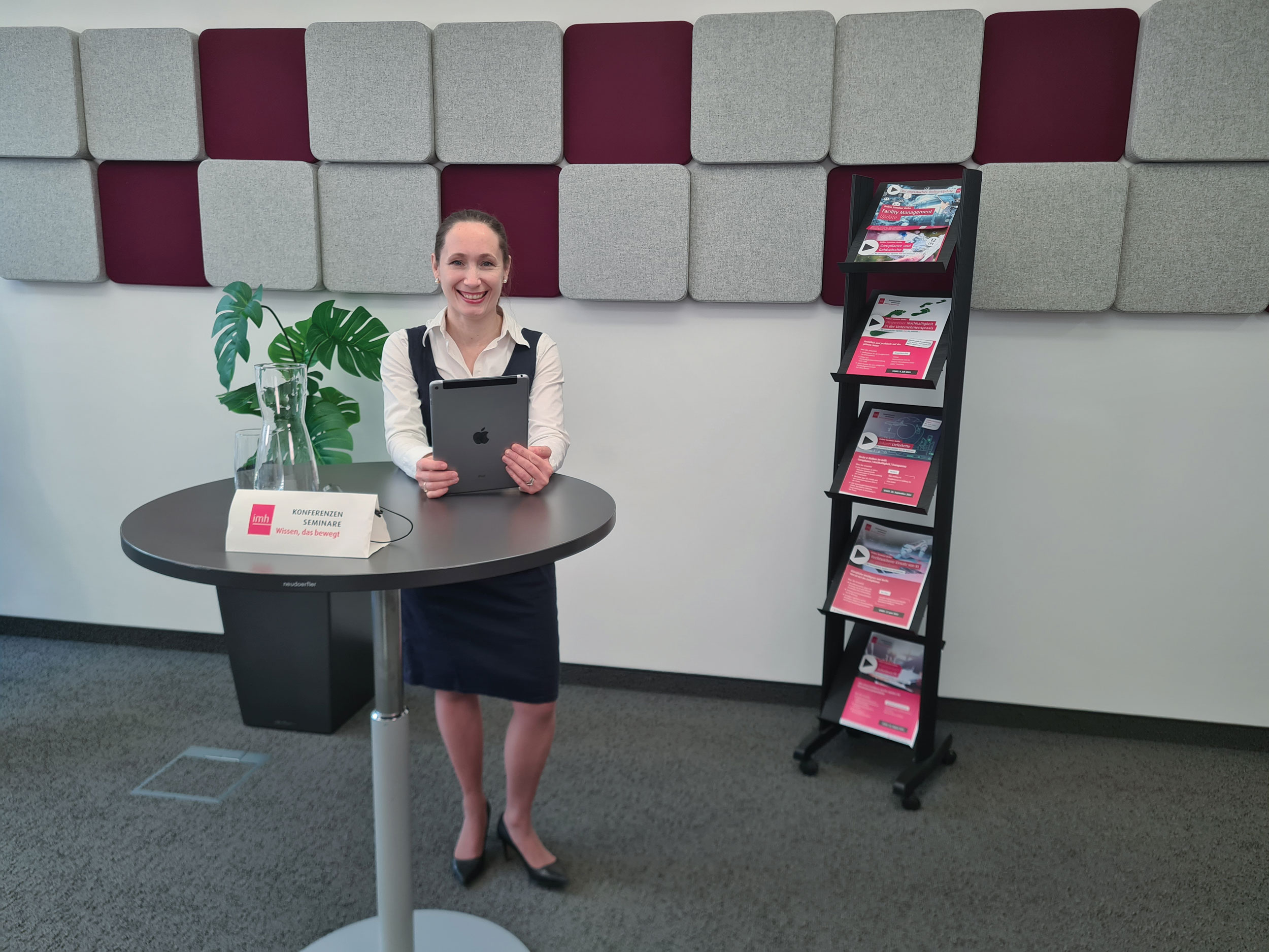 Eine Frau mit einem Tblett steht bei einem Stehtisch im imh Online Studio.