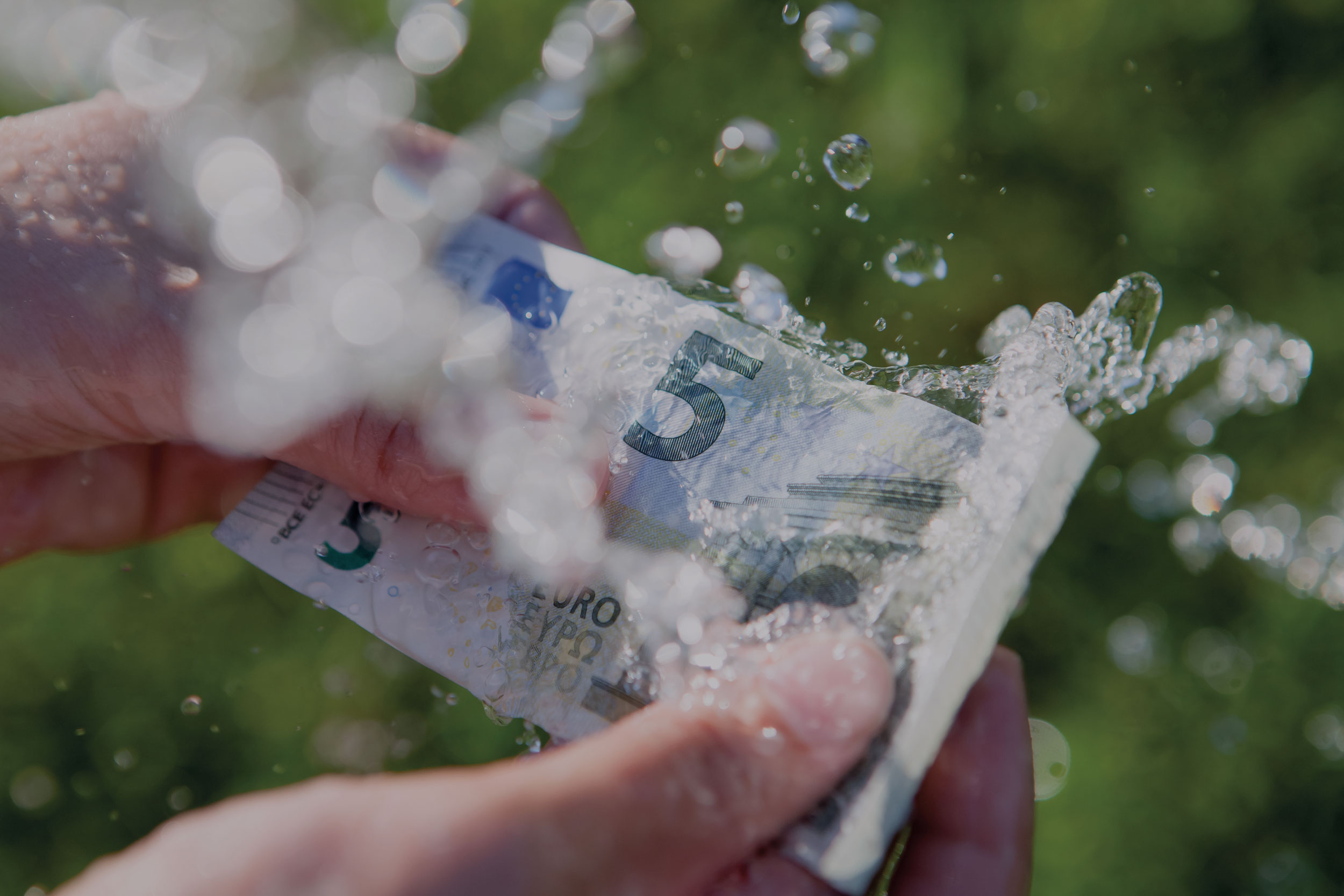Ein 5 Euroschein der in der HAnd gehalten wird, wird mit Wasser bekippt.