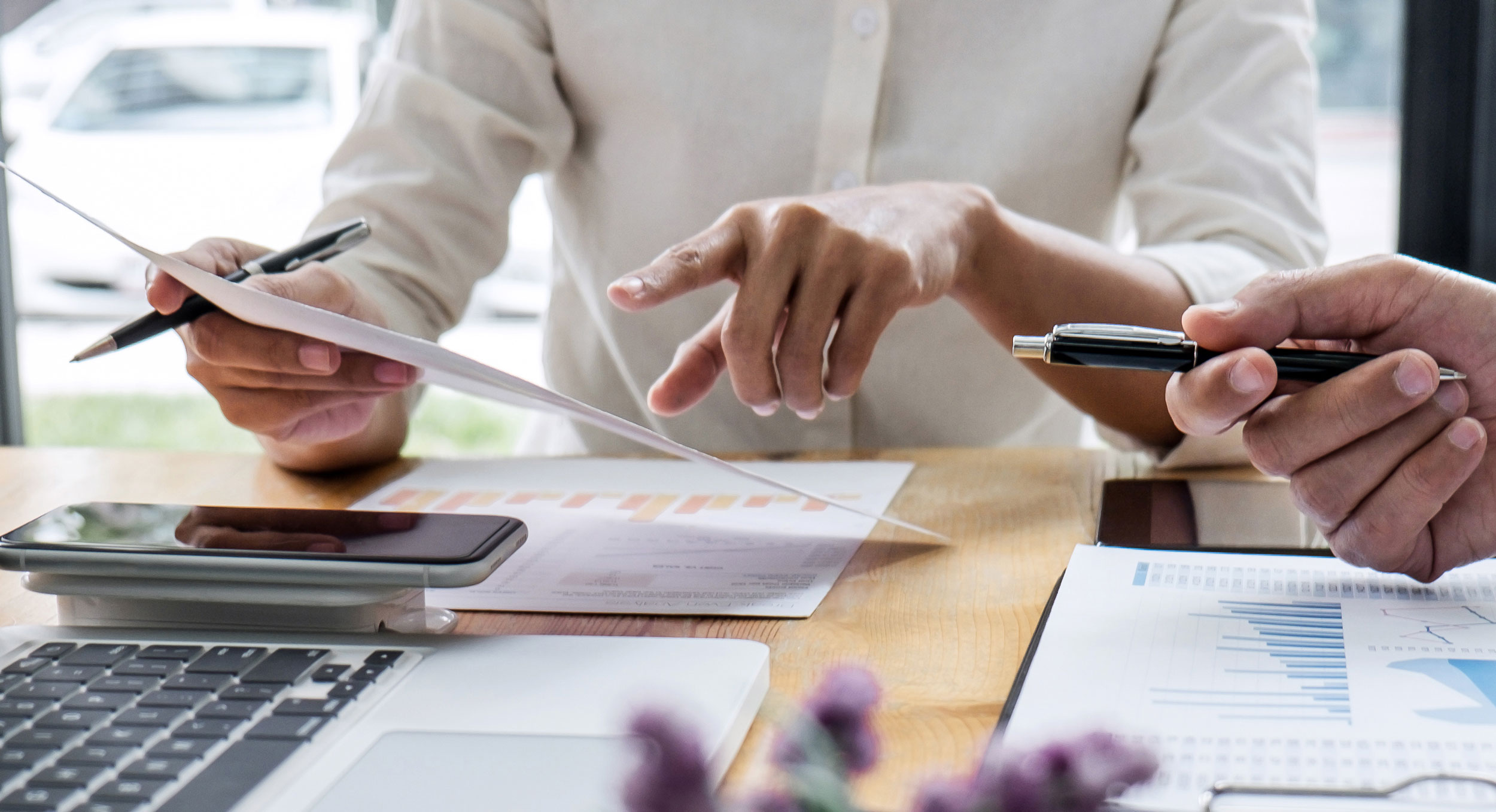 2 Personen in einem Metting, die gemeinsam Analysen anschauen. auf dem Tischin der mitte liegen mehere Bläter mit Charts, ein Laptop und 2 Tabletts. 