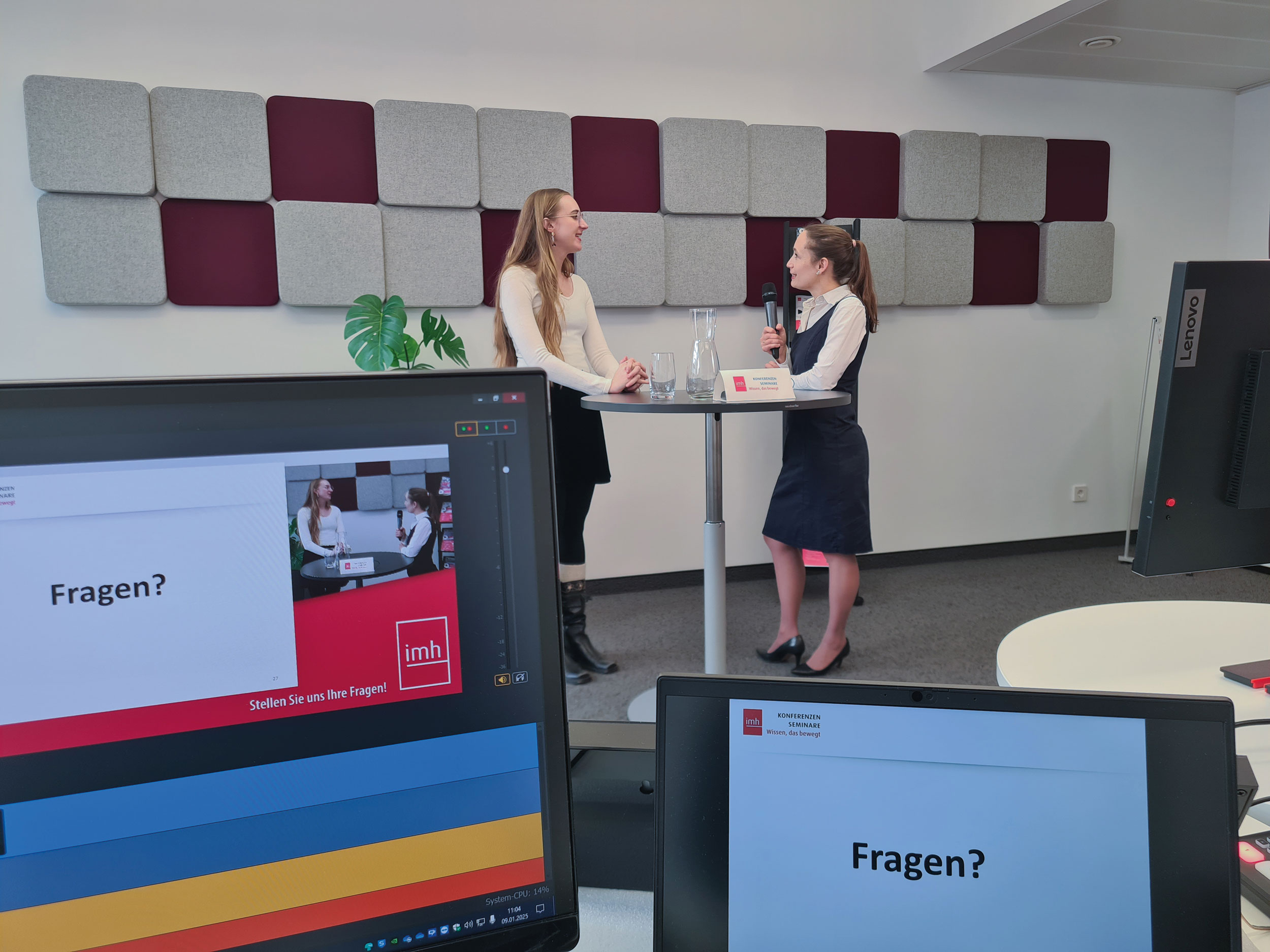 Im Vordergrund sind Bildschirme, auf einem steht "Fragen?". Im Hintergrund ist eine Interviewsituatuion bei der eine Frau einer anderen eine Frage stellt.