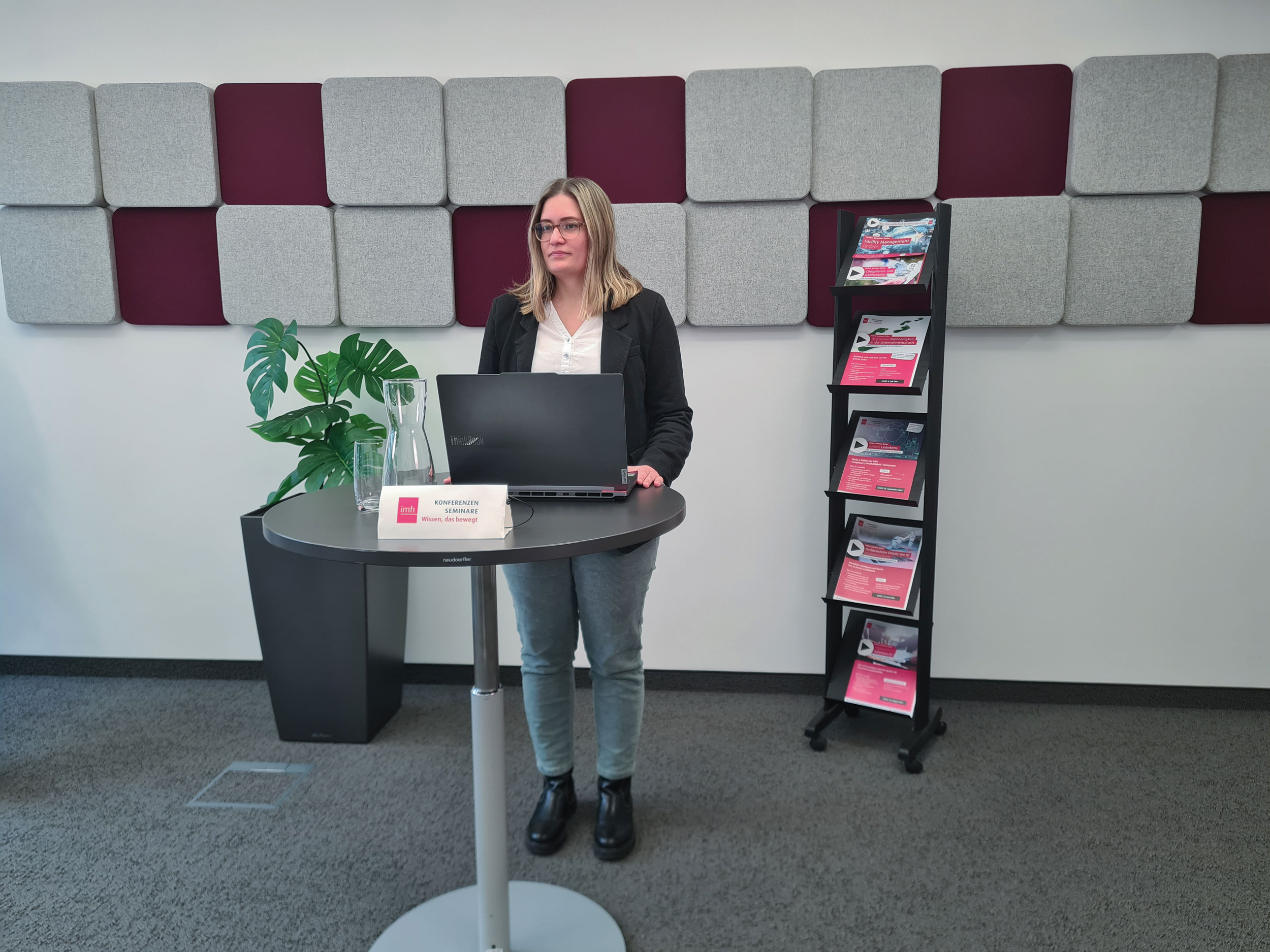 Eine Frau mit einem Laptop steht bei einem Stehtisch im imh Online Studio.