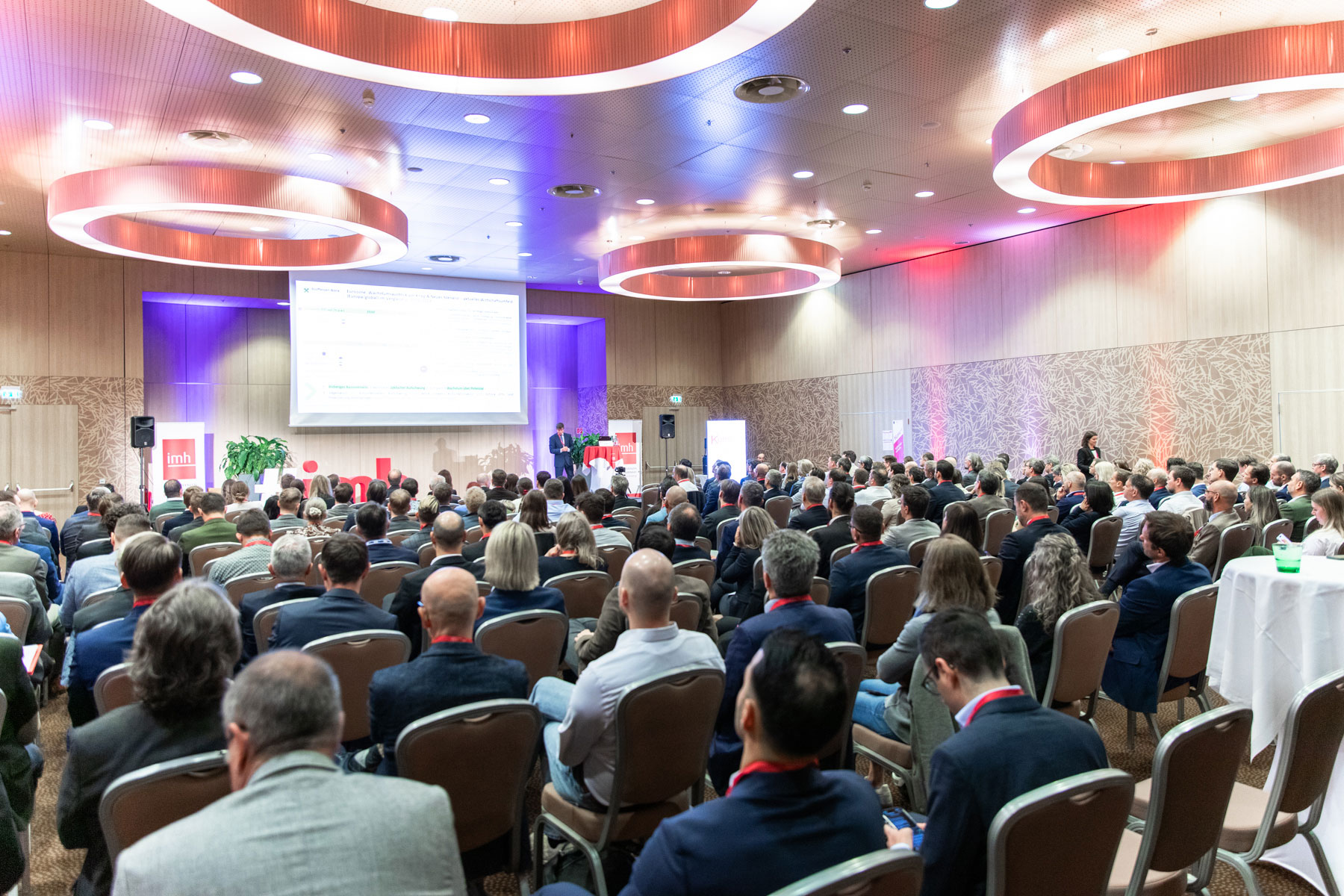 Ein voller Konferenzraum mit Vortragendem vor Publikum