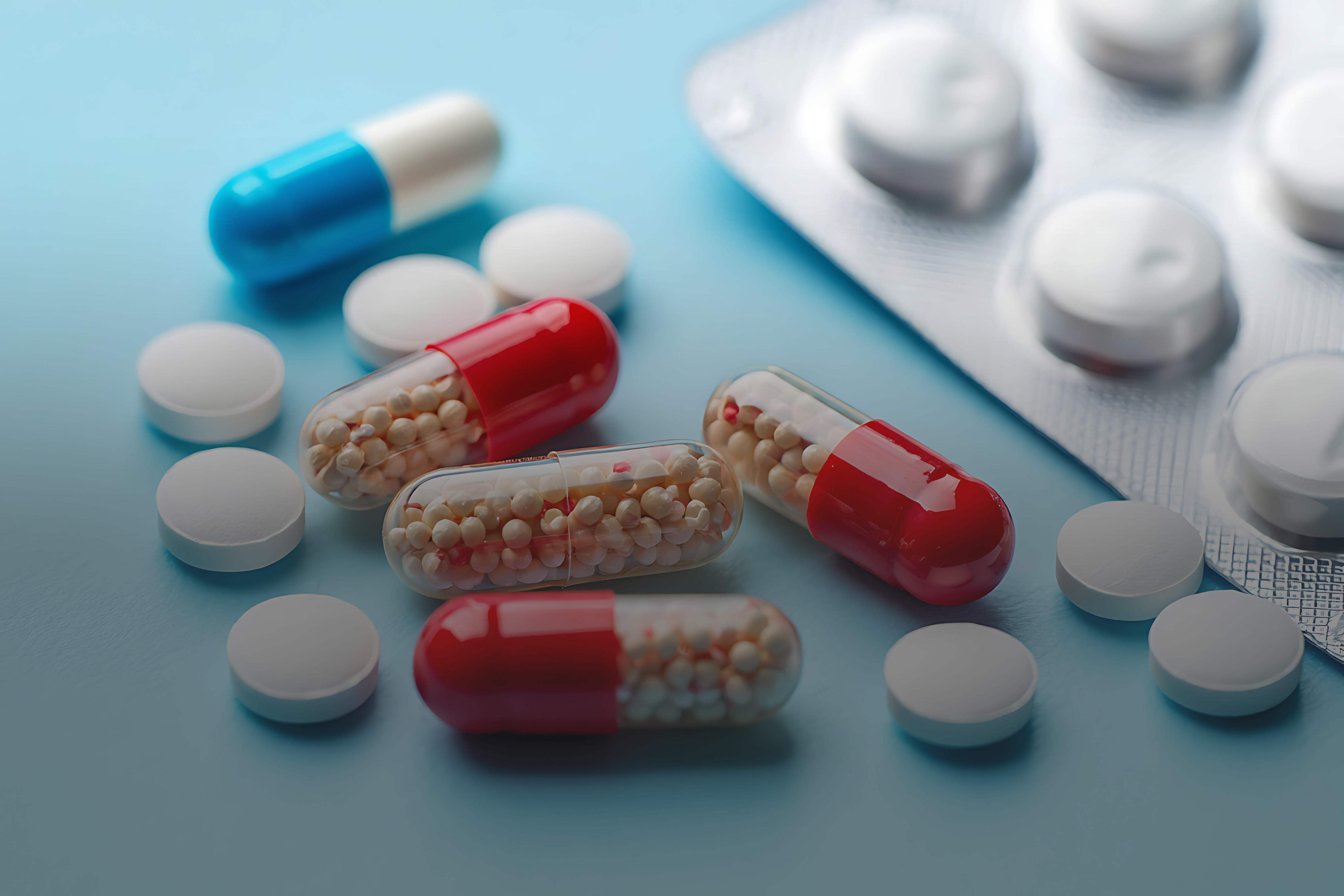 Tabletten und Pillen auf einem hellblauen Untergrund, daneben eine Blisterverpackung