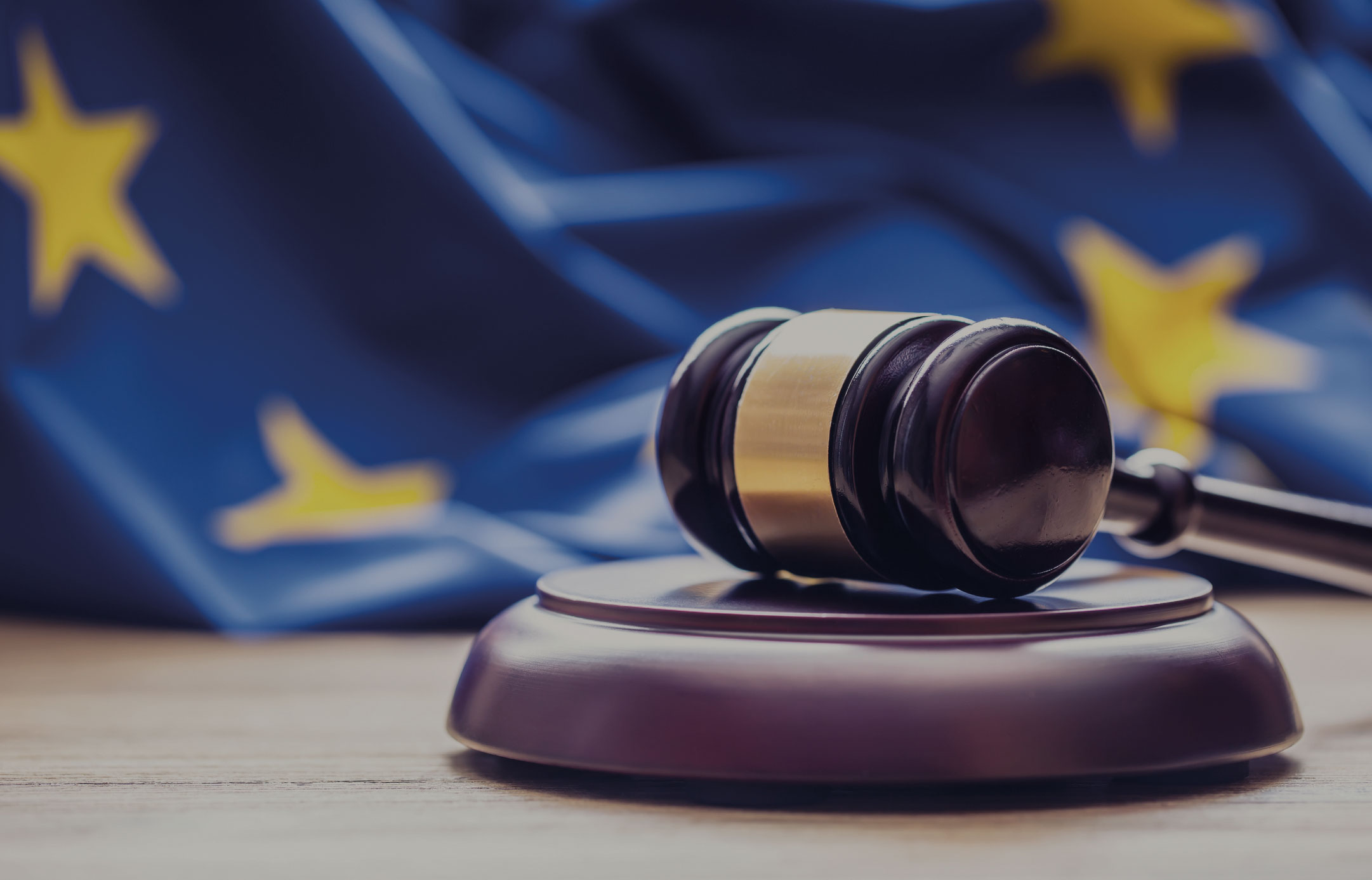 Ein Richterhammer auf einem Tisch. Im Hintergrund ist eine EU Flagge.